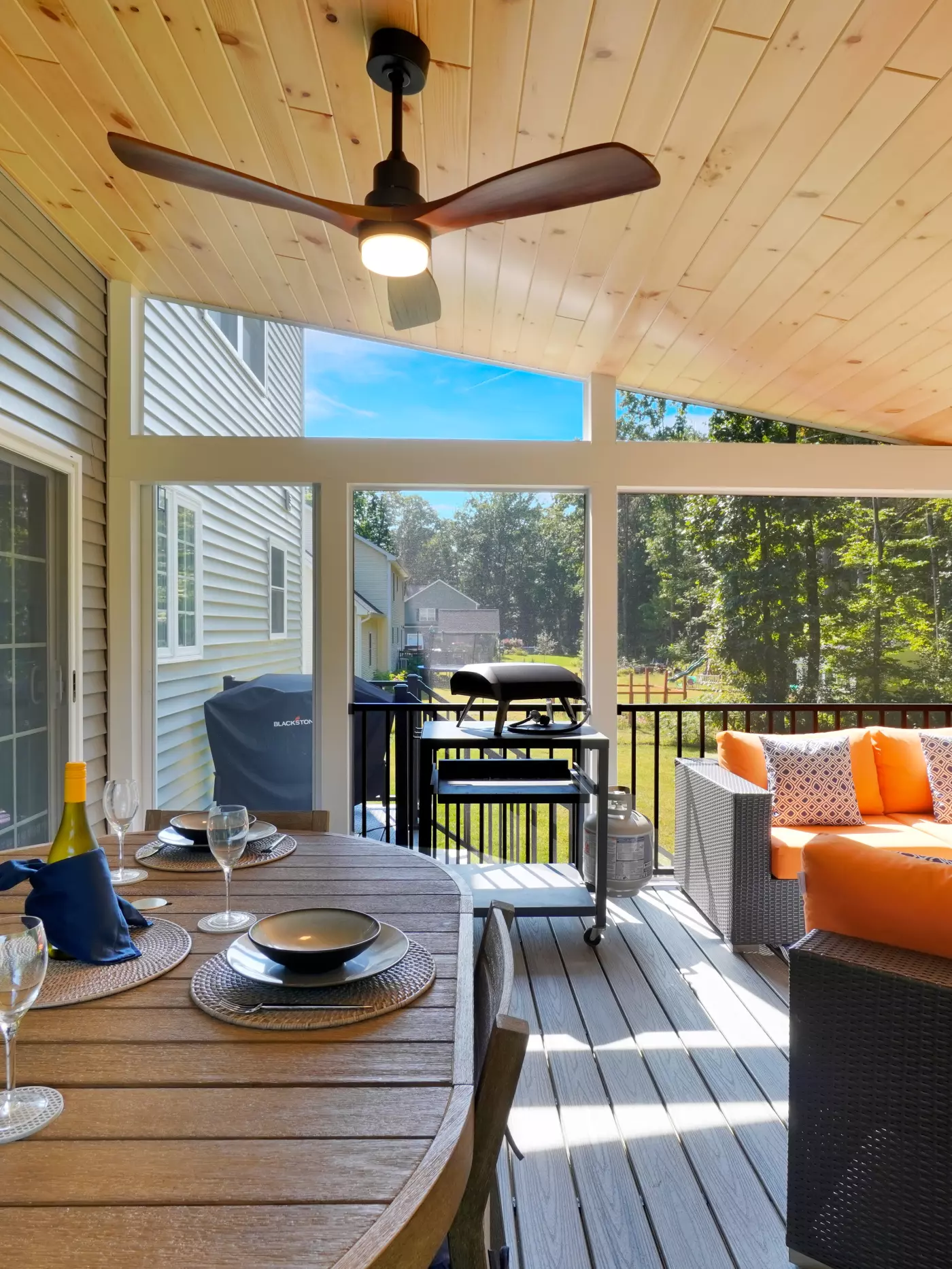 Inviting screened porch with dining area, grill, and cozy seating amidst greenery.