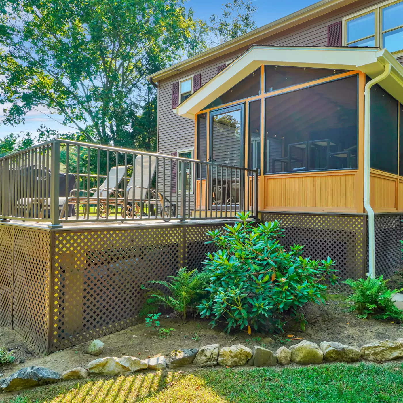 A modern deck with a screened porch, surrounded by greenery and landscaping.
