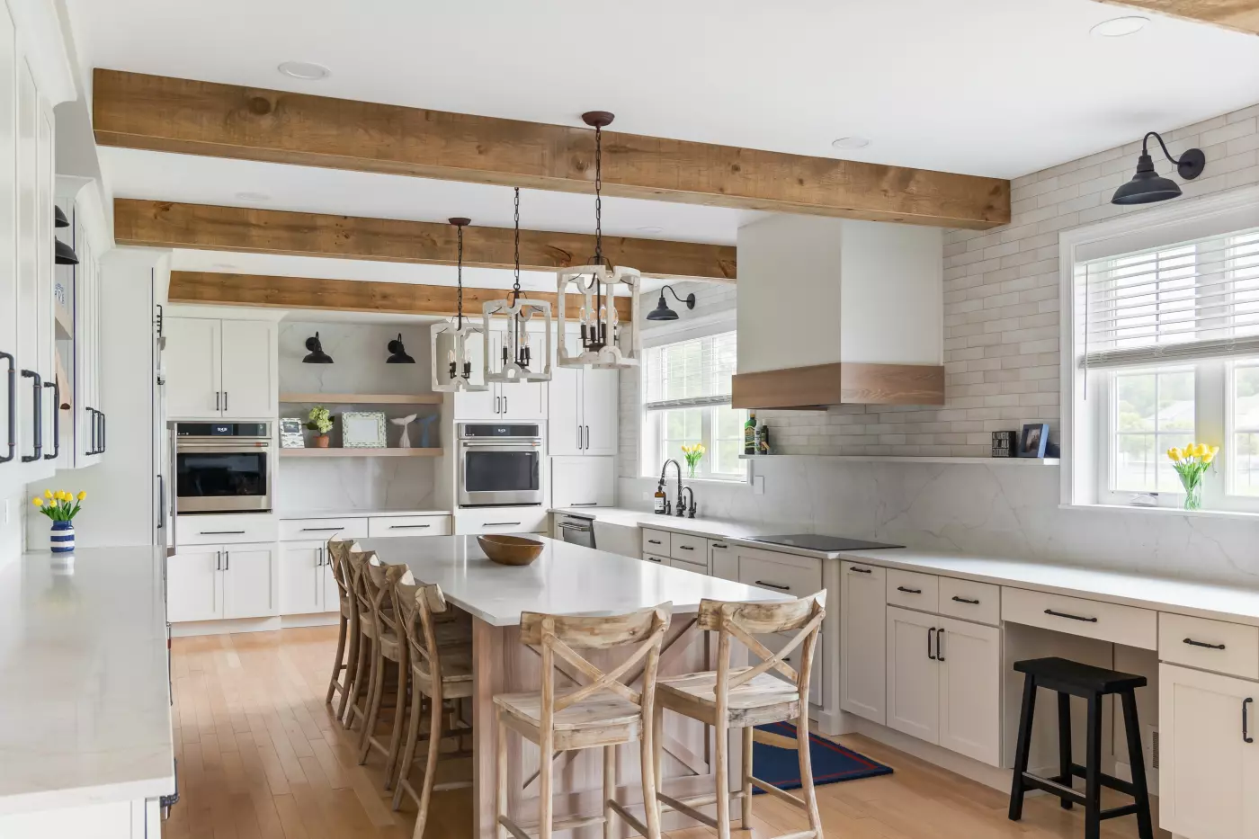 Modern farmhouse kitchen with wood ceiling beams, oversized island, white cabinets, and rustic pendant lights.