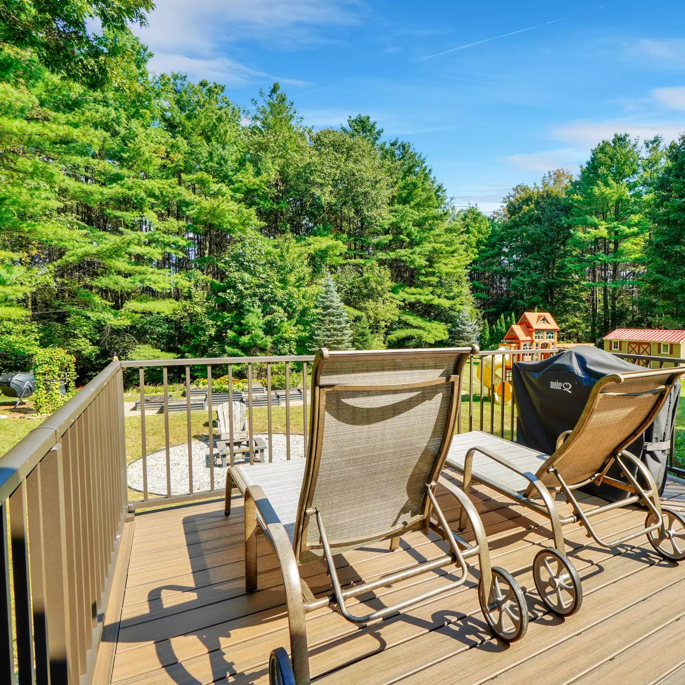 Two lounge chairs on a deck overlooking a green, forested backyard.