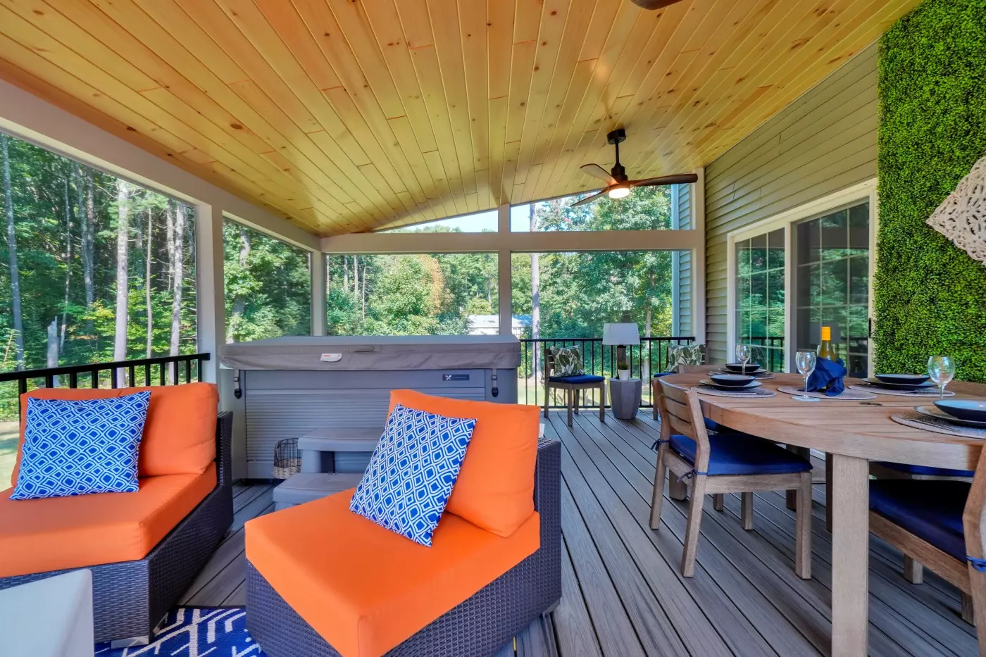 Screened porch featuring orange seating, wood dining furniture, hot tub, vaulted wood ceiling, and forest views.