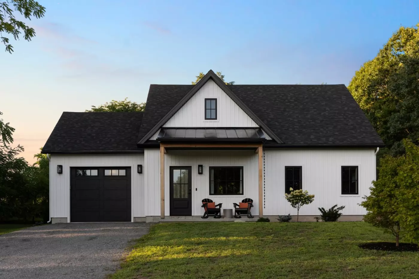 Modern white house with a black roof, front porch, and two chairs on the lawn.