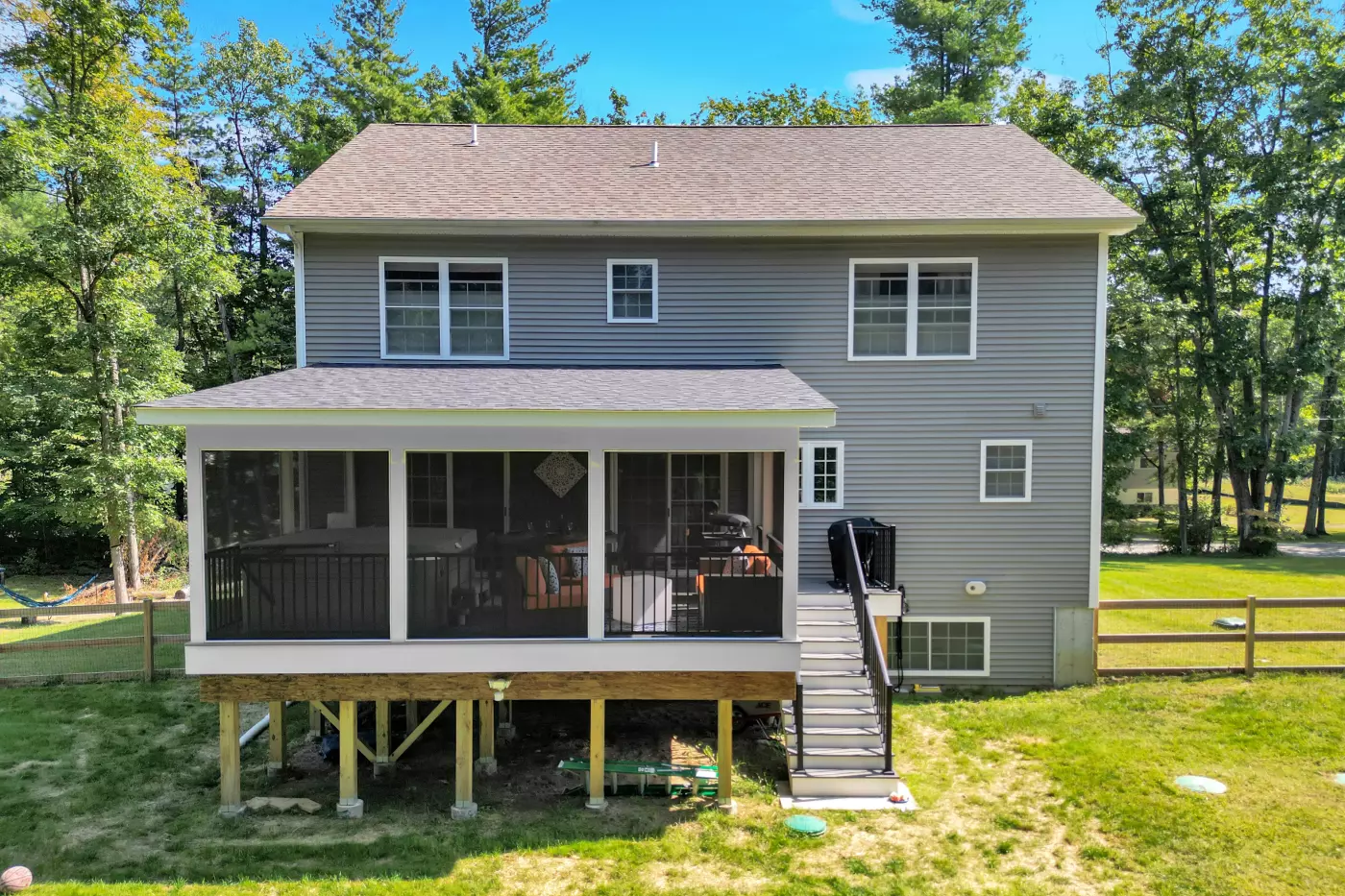 A two-story gray house with a screened porch and stairs, surrounded by trees and grass.