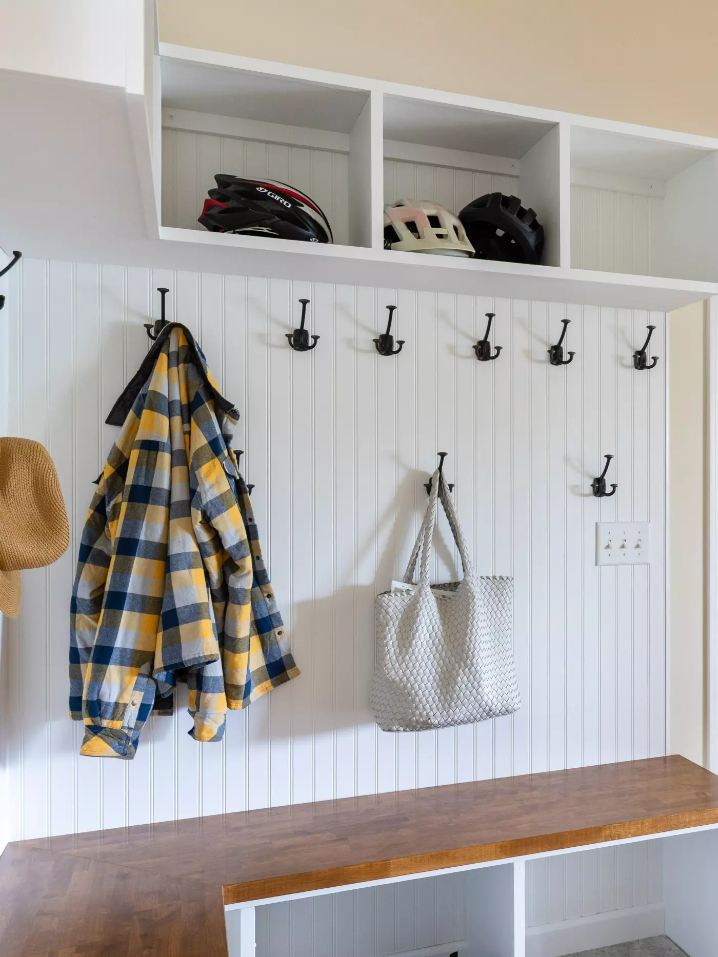 Mudroom with hooks for jackets and helmets, a bench, and a patterned tote bag.