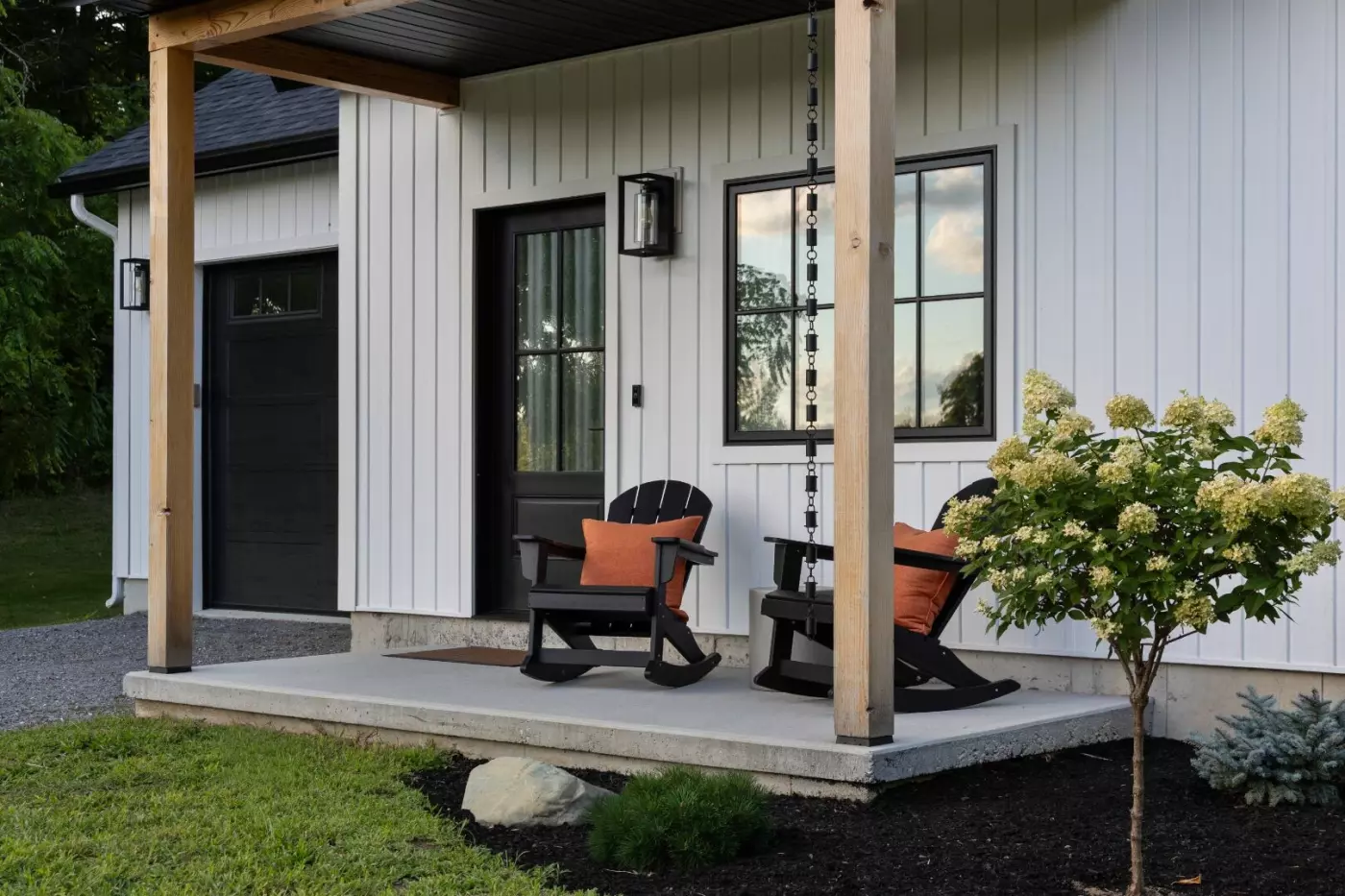 Cozy porch with black rocking chairs, orange cushions, and a flowering bush.
