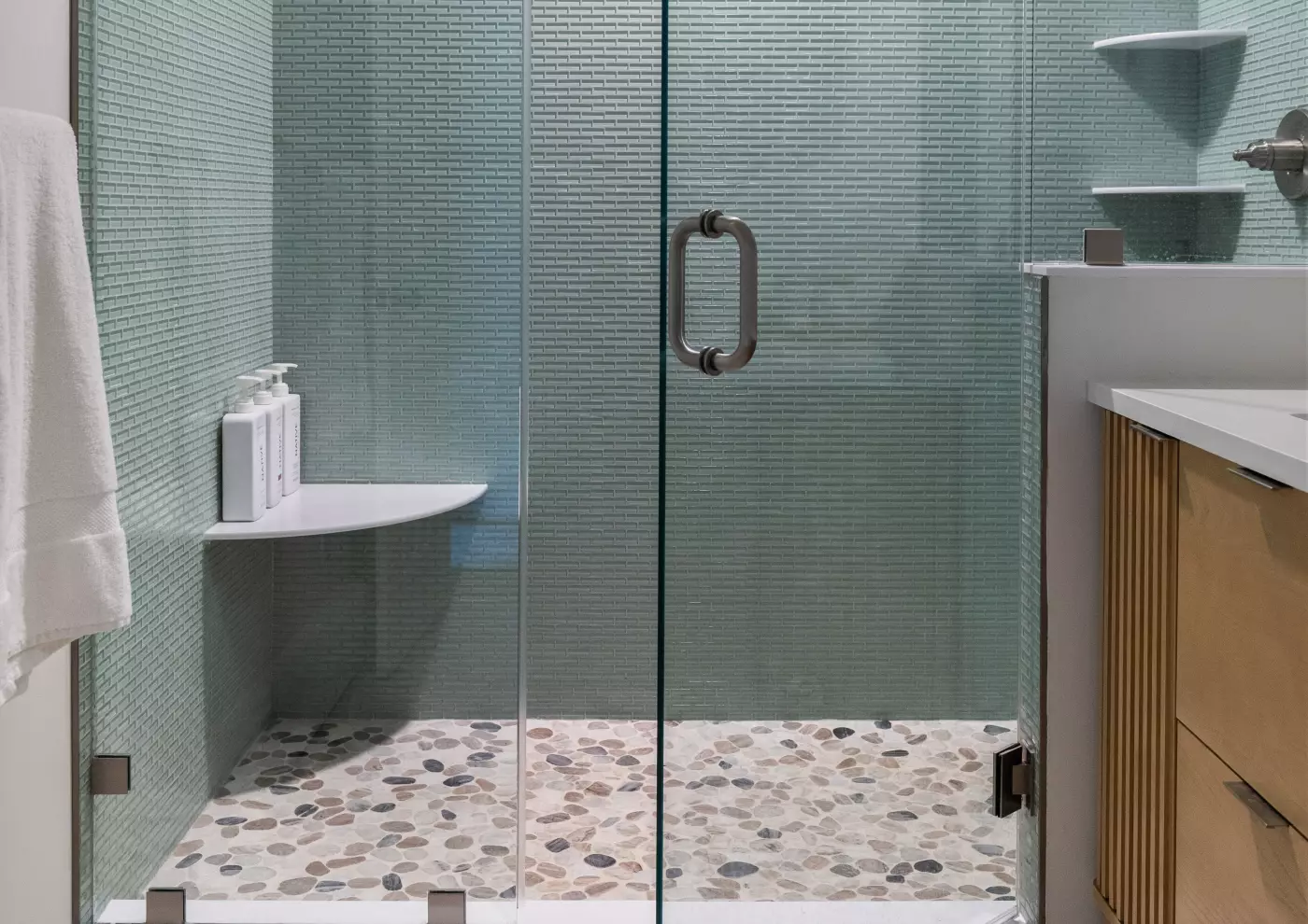 Modern glass shower with green tiled walls and a pebble stone floor.