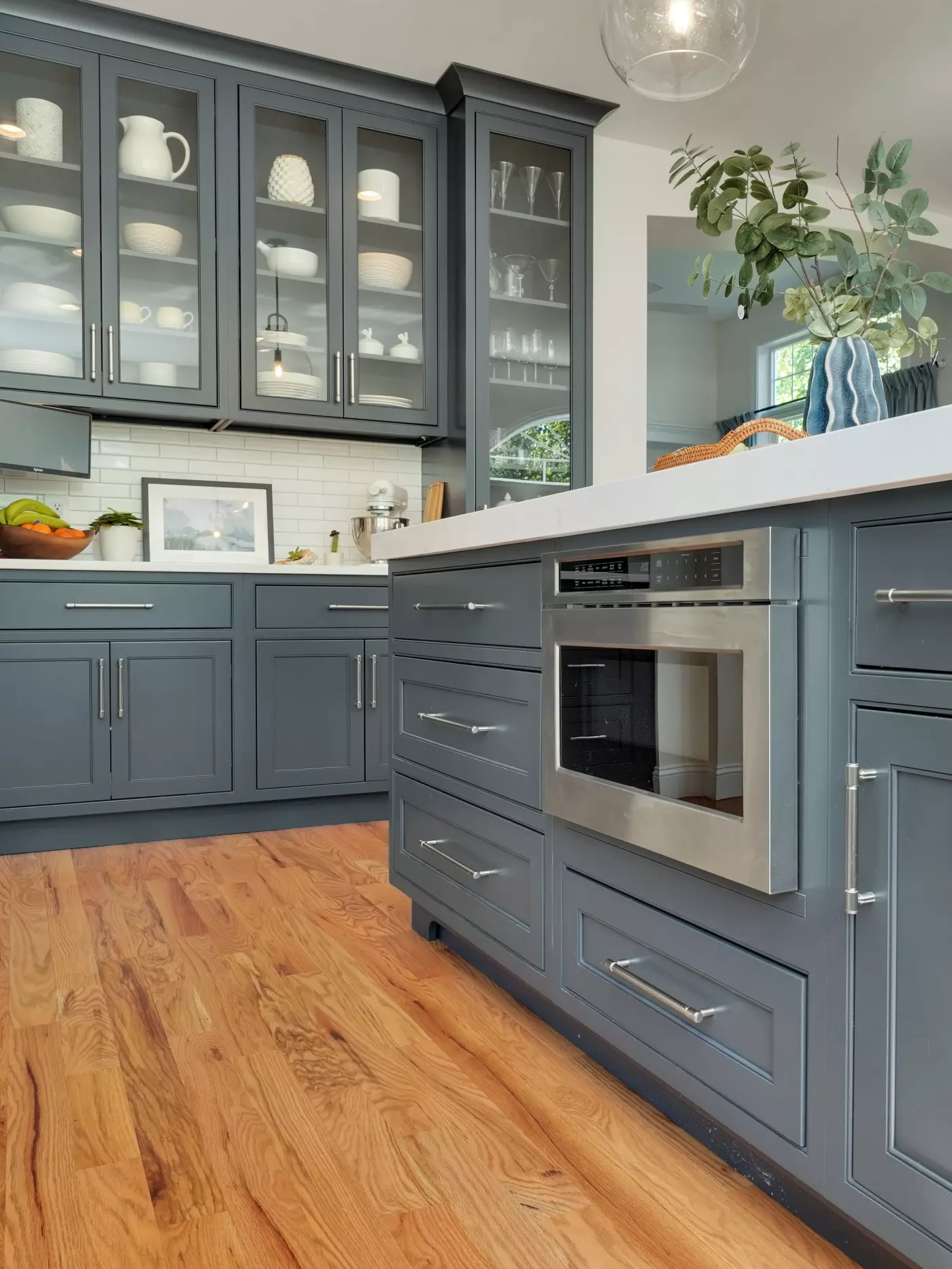 Modern kitchen with gray cabinetry, glass doors, and wooden flooring.