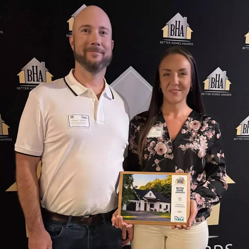 Two people pose together at an awards event, holding a home award plaque.
