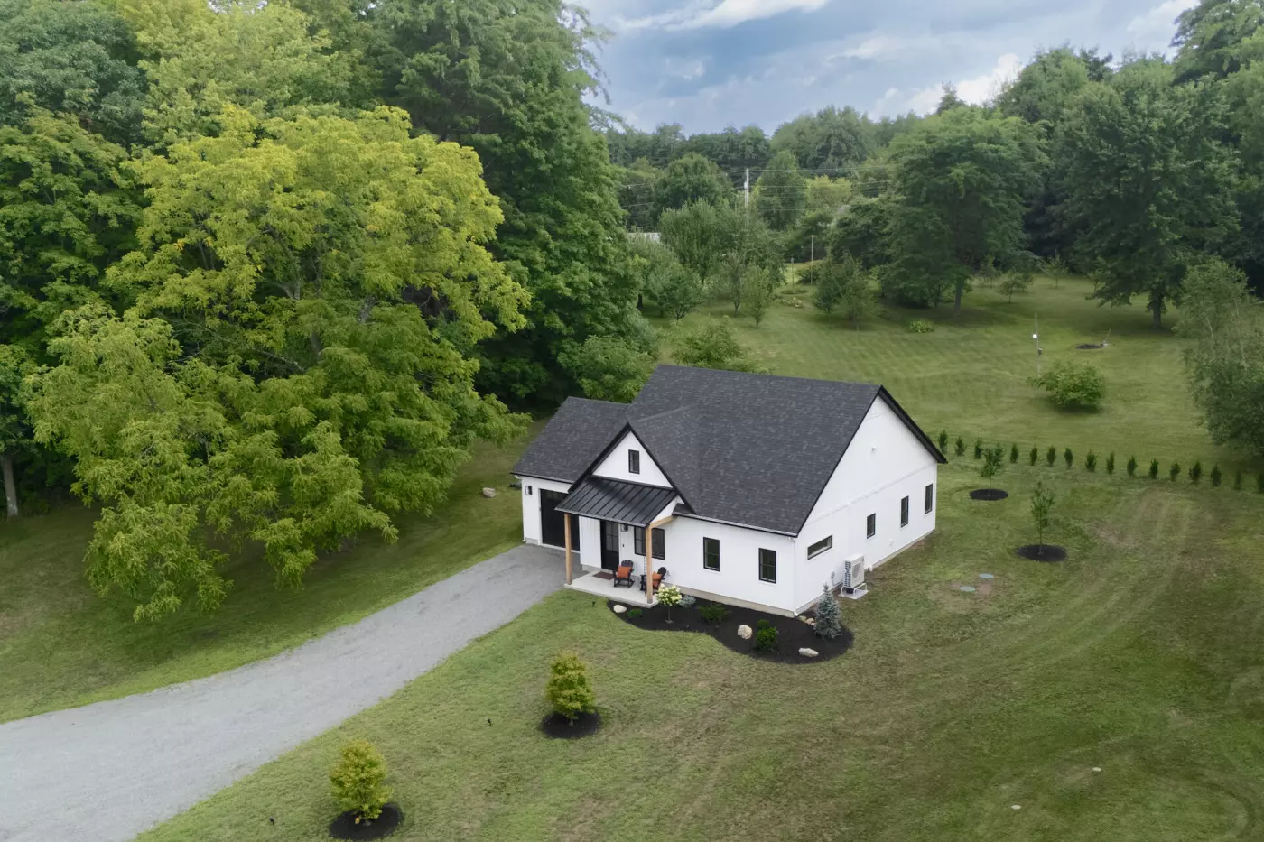 Aerial view of a modern white house surrounded by lush green trees and landscaped yard.