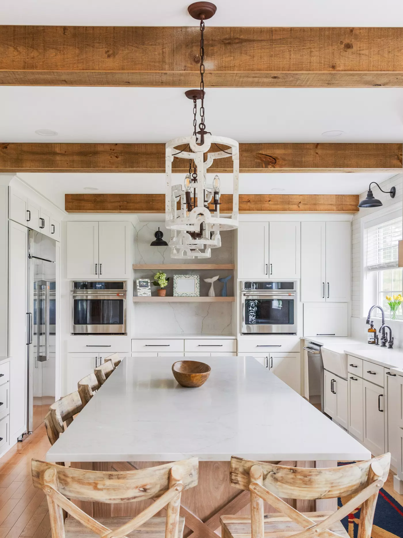 Modern kitchen with wooden beams, white cabinets, and a large marble island.