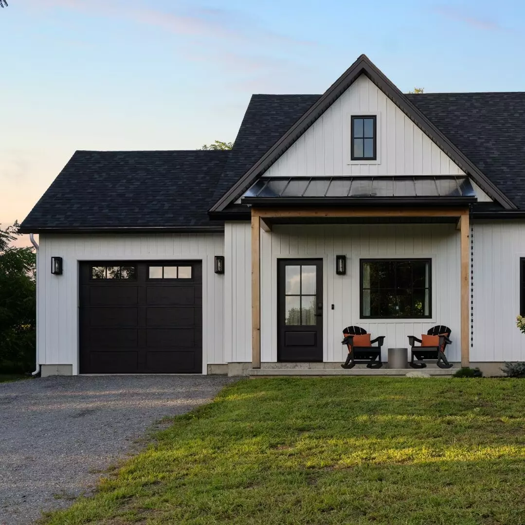 Modern white house with a black roof, featuring a porch and two rocking chairs.