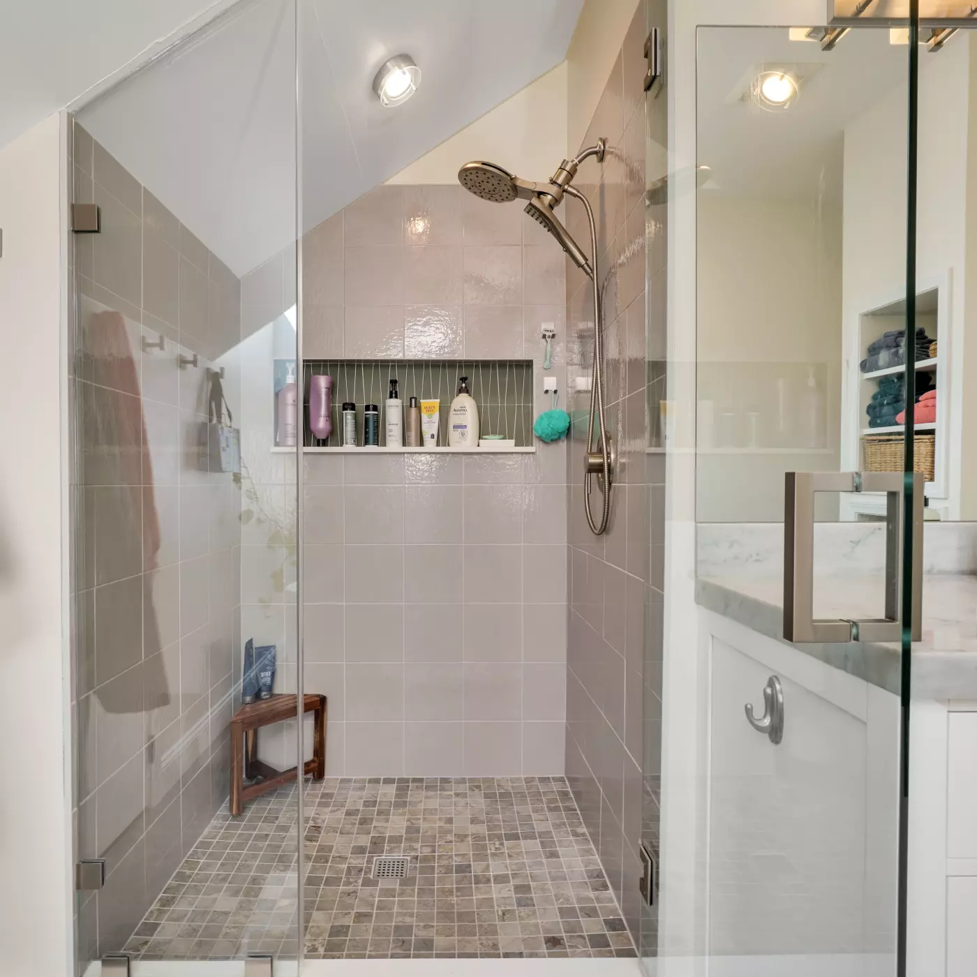 Modern shower with a glass door, tiled walls, and various toiletries on a shelf.