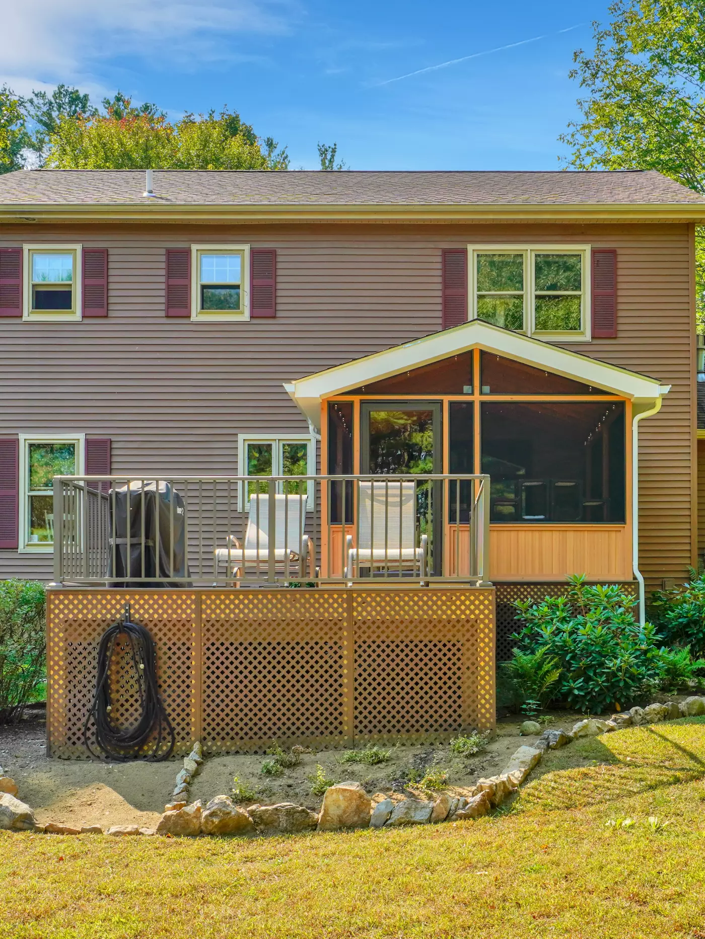 Backyard view of a house with a screened porch and wooden deck.