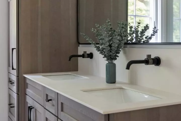 Modern bathroom vanity with two sinks, a mirror, and a vase of greenery.