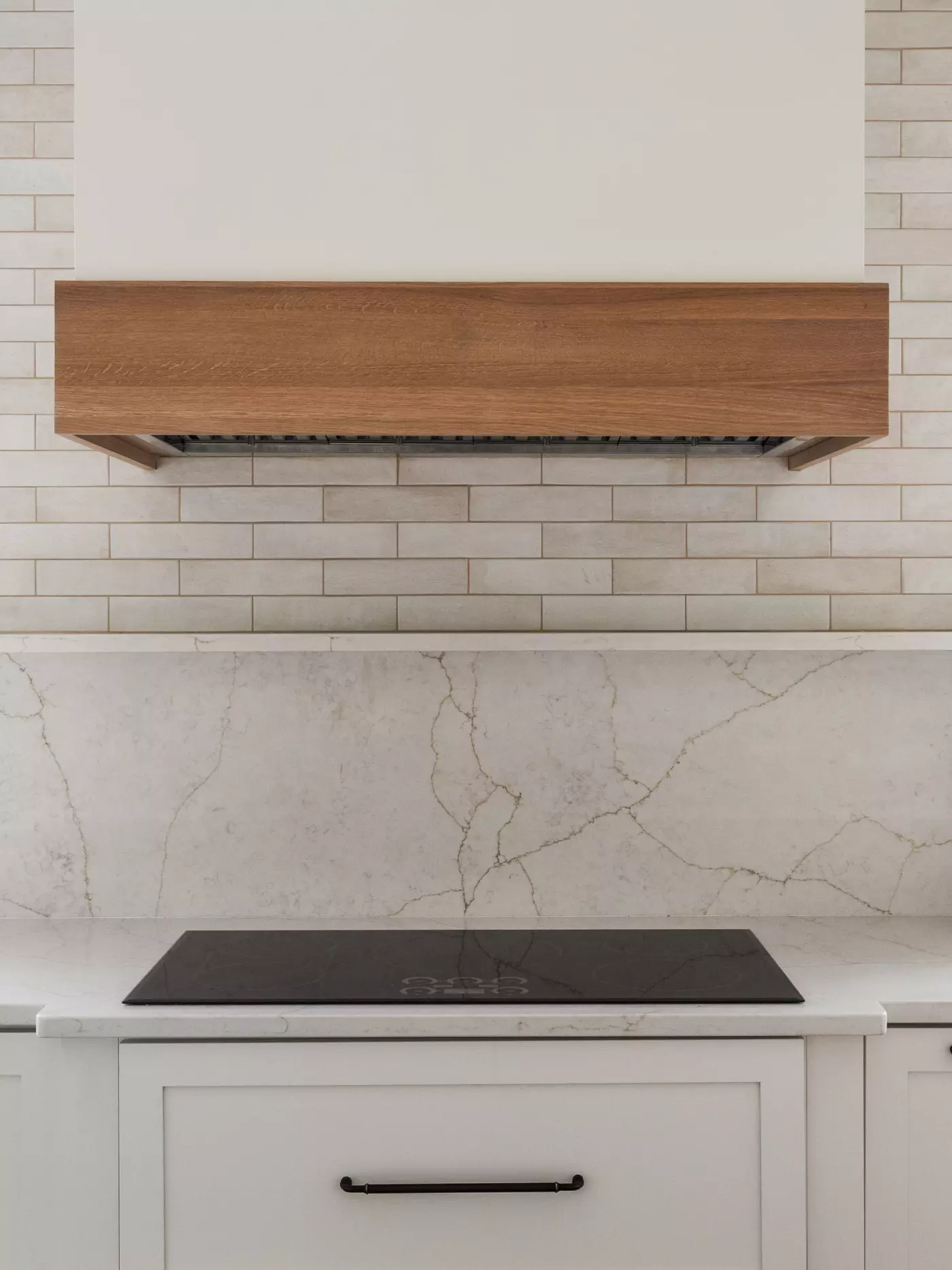 Modern kitchen with a wooden range hood, marble backsplash, and a black cooktop.