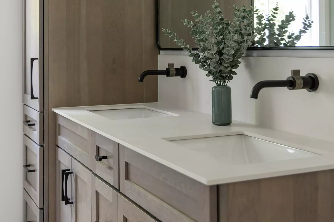 Double-sink bathroom vanity with light wood cabinetry, black wall-mounted faucets, and a large framed mirror.
