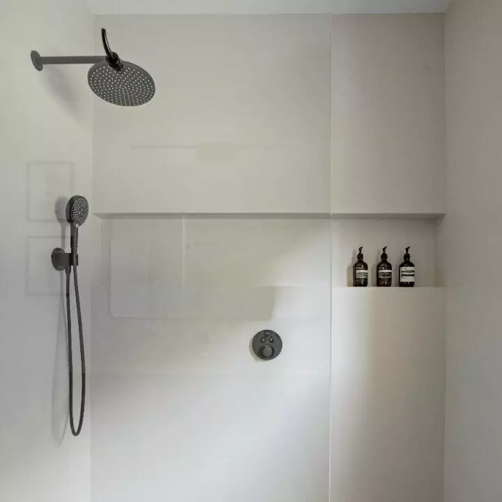 Modern shower with black fixtures and a shelf holding three bottles.