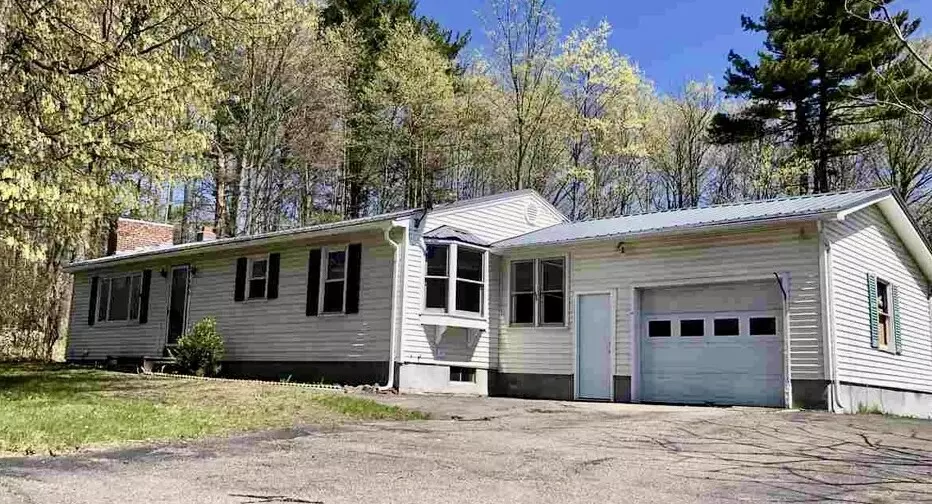 Single-story white house with a garage, surrounded by trees and greenery.