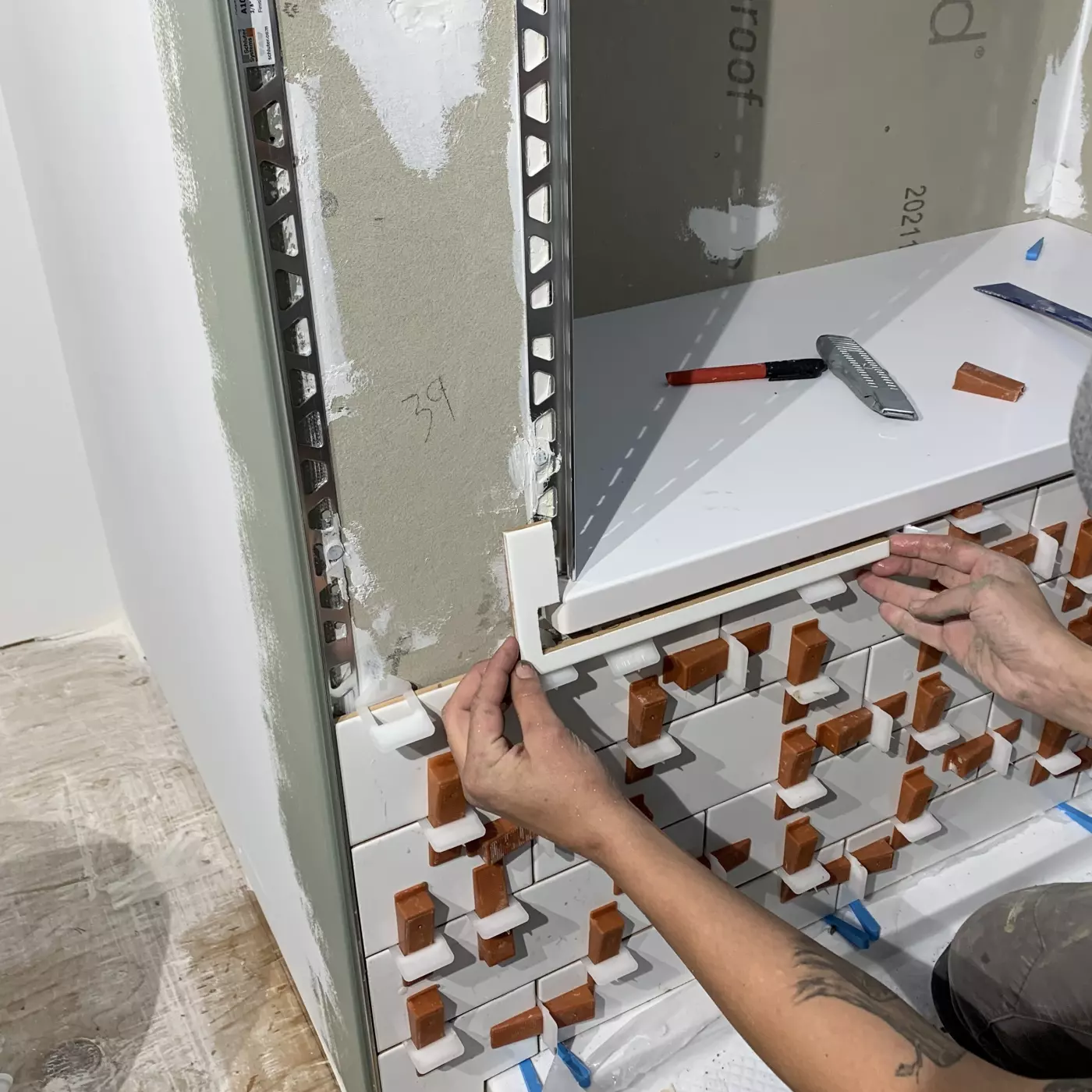 A person installs trim on tiled wall during renovation work.
