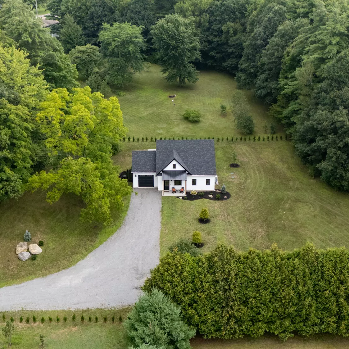 Aerial view of a white house surrounded by greenery and a gravel driveway.