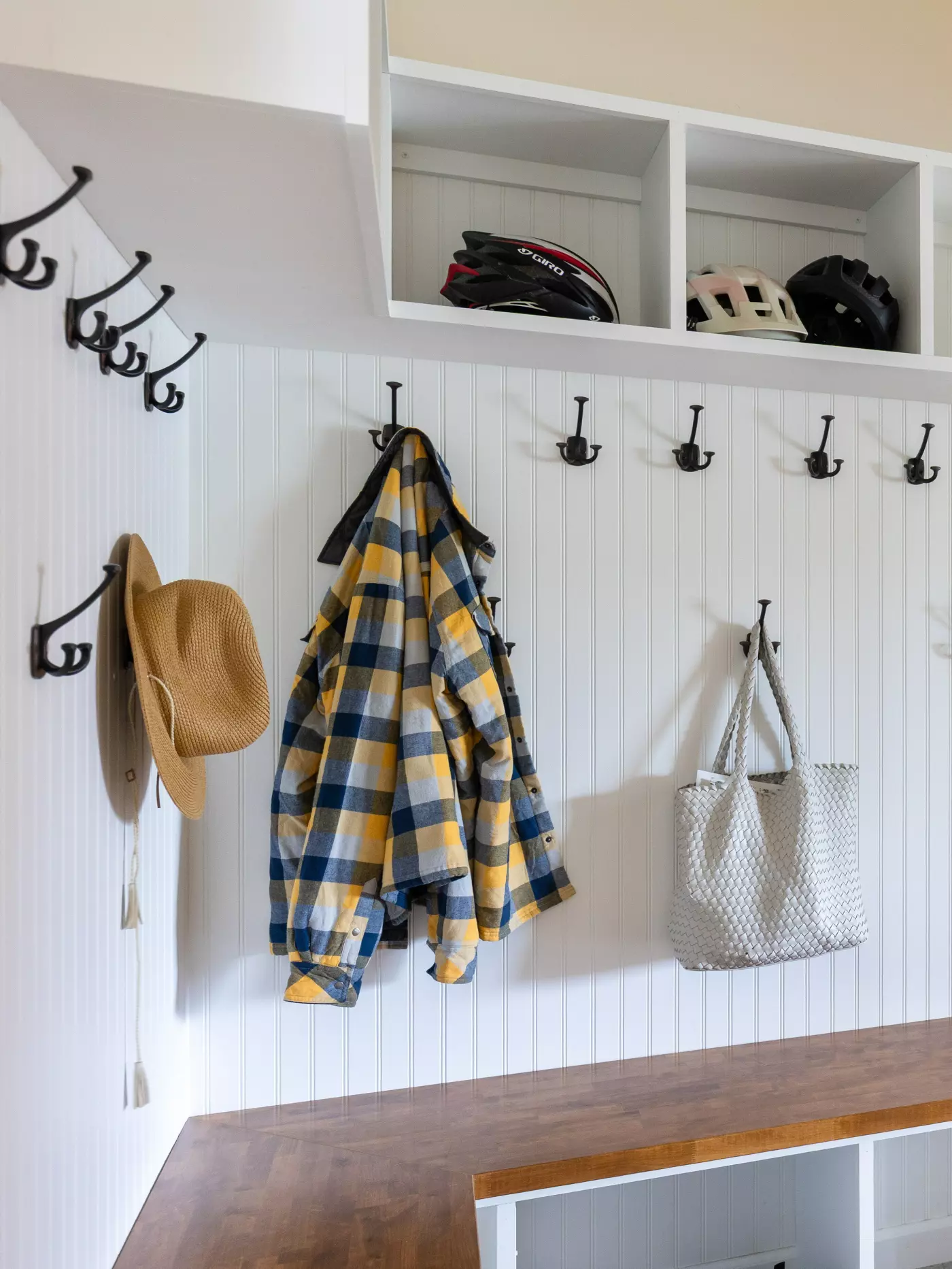 A cozy entryway with hooks, a plaid jacket, hats, helmets, and a woven bag.