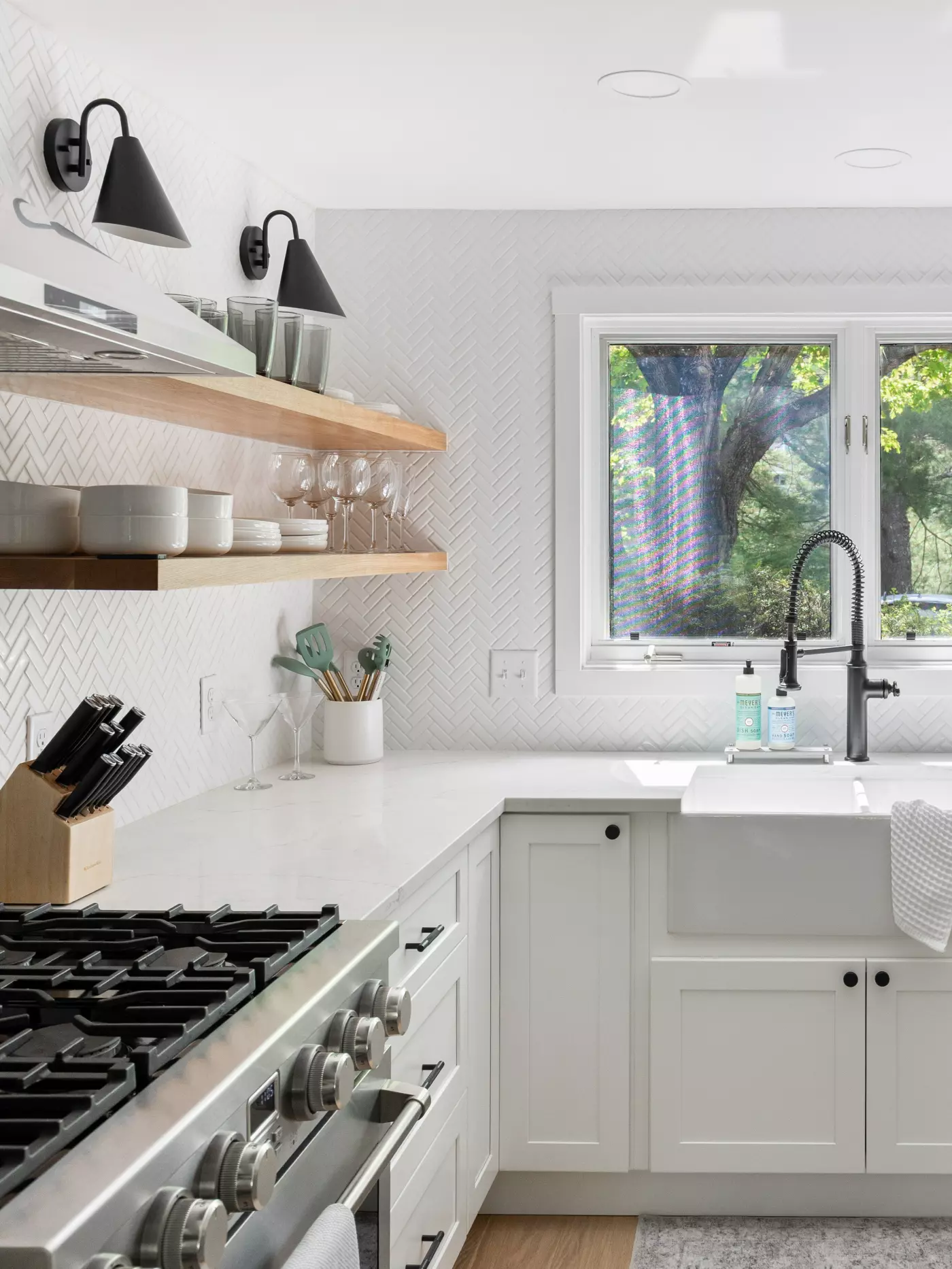 Modern kitchen with herringbone backsplash, open shelves, and large sink.