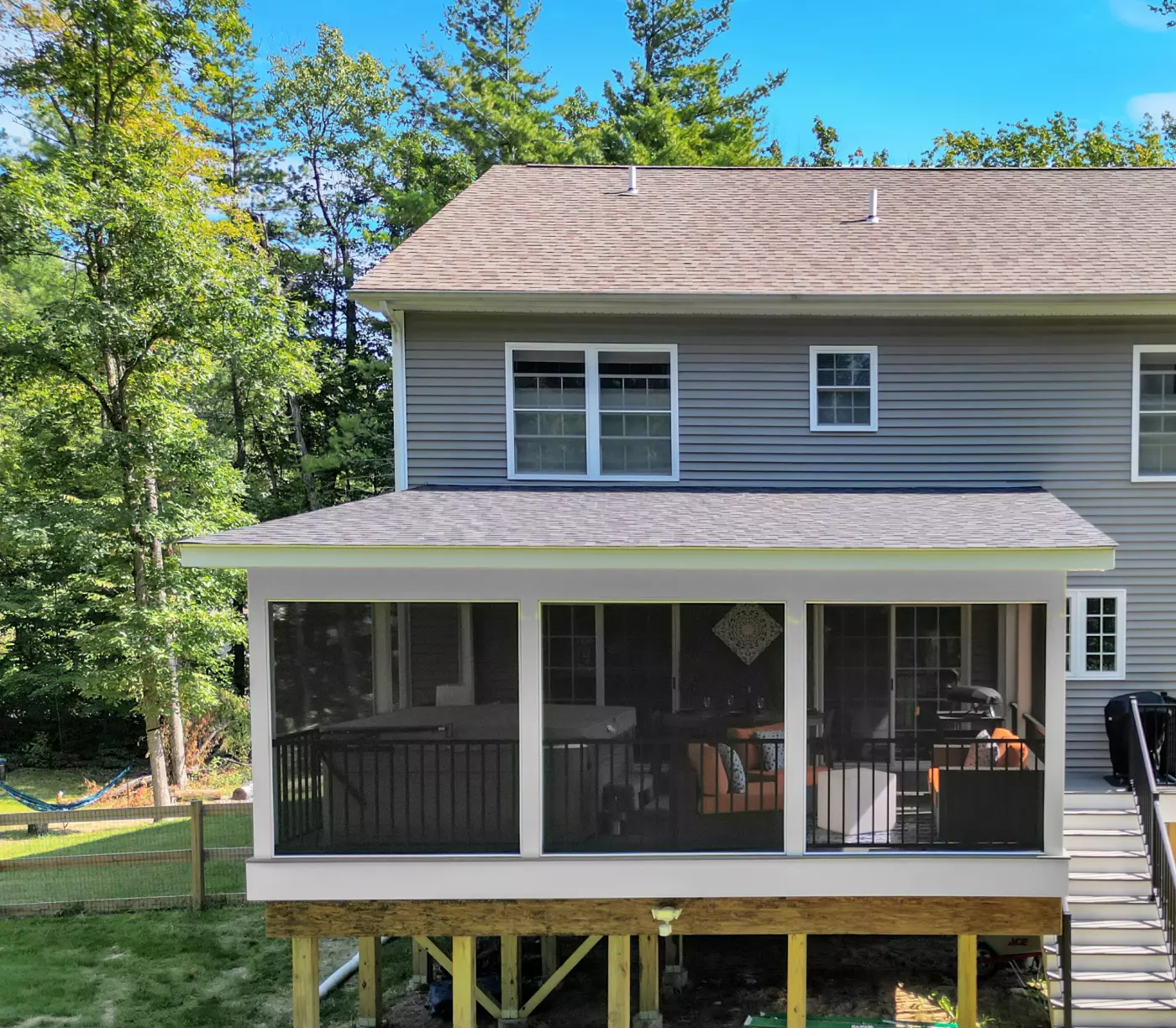 Back view of a house featuring a screened porch and wooded backdrop.