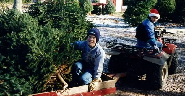 Taylor Sears and friend transporting a Christmas tree on a small trailer, with a snowy background.