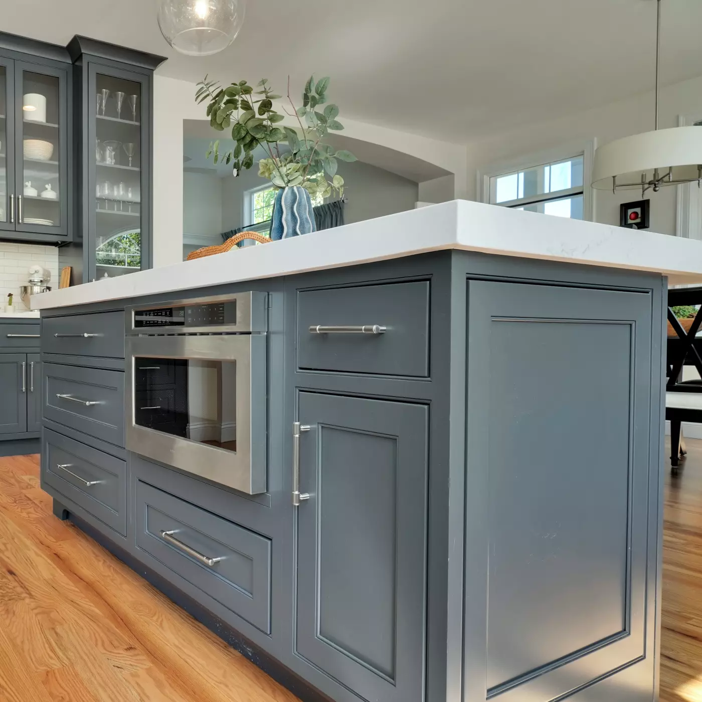 Modern kitchen island with gray cabinets and a marble top, featuring a microwave and plants.