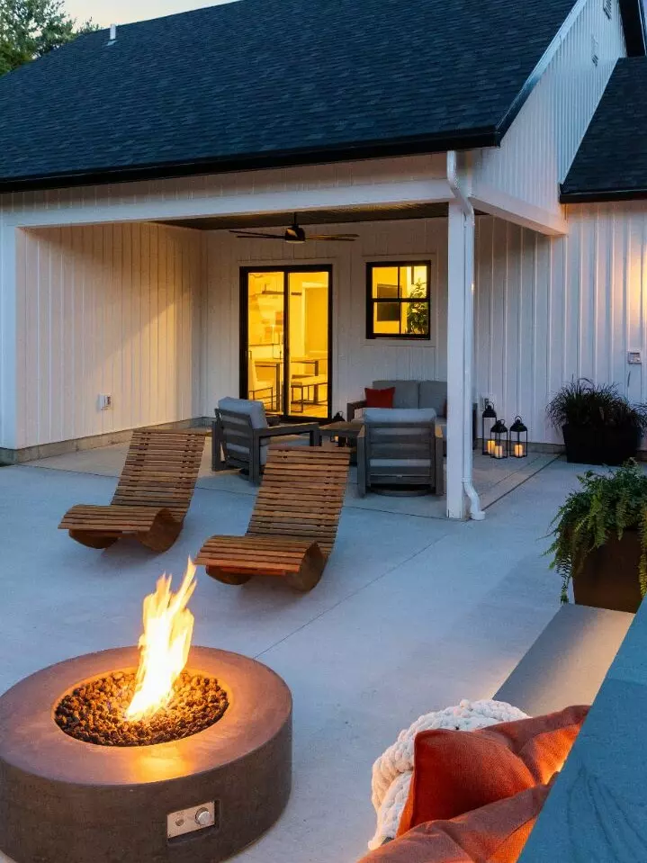 Modern outdoor patio with a fire pit, lounge chairs, and warm ambient lighting.