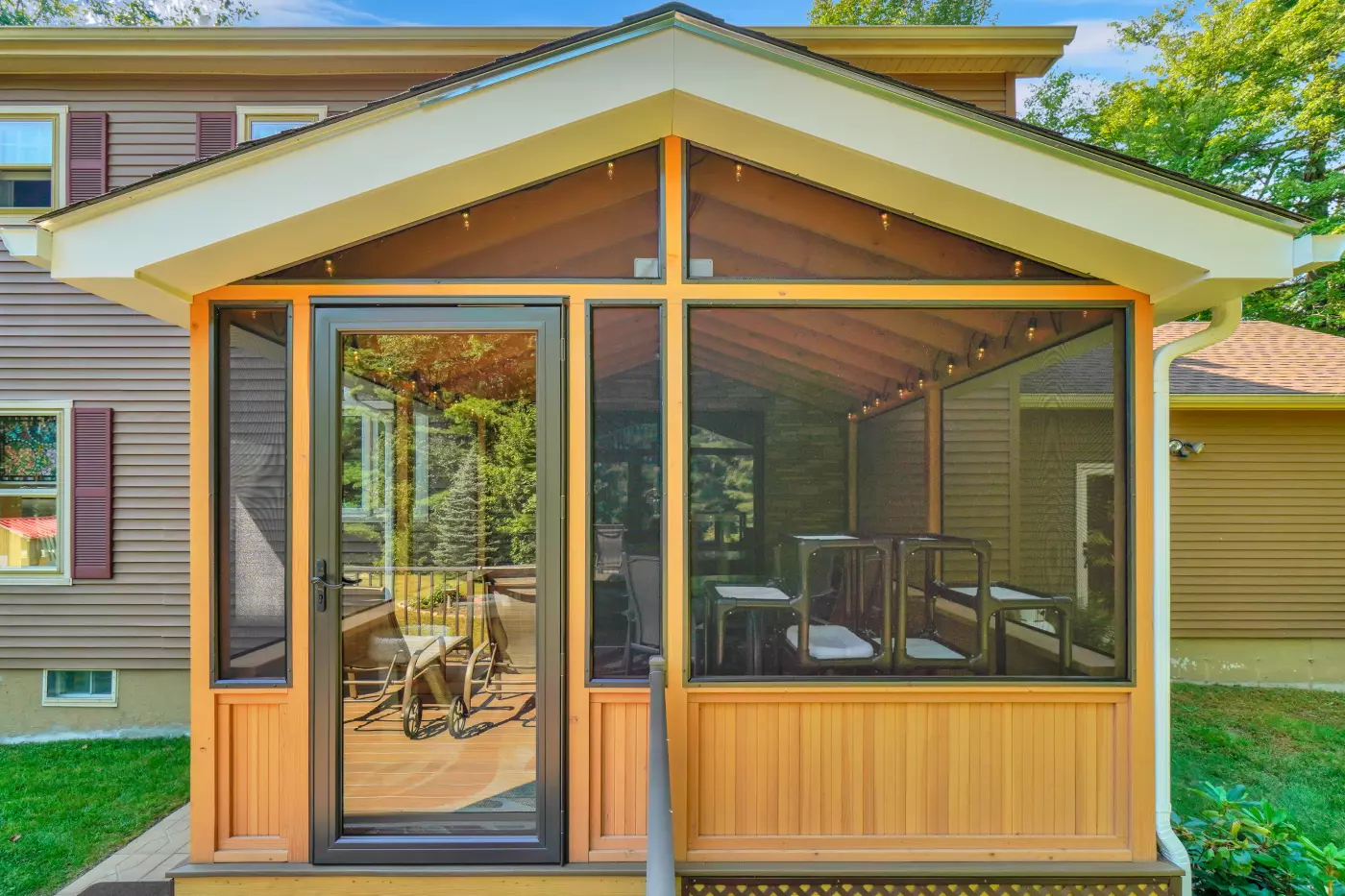 Screened porch with wooden frame and chairs, surrounded by greenery.