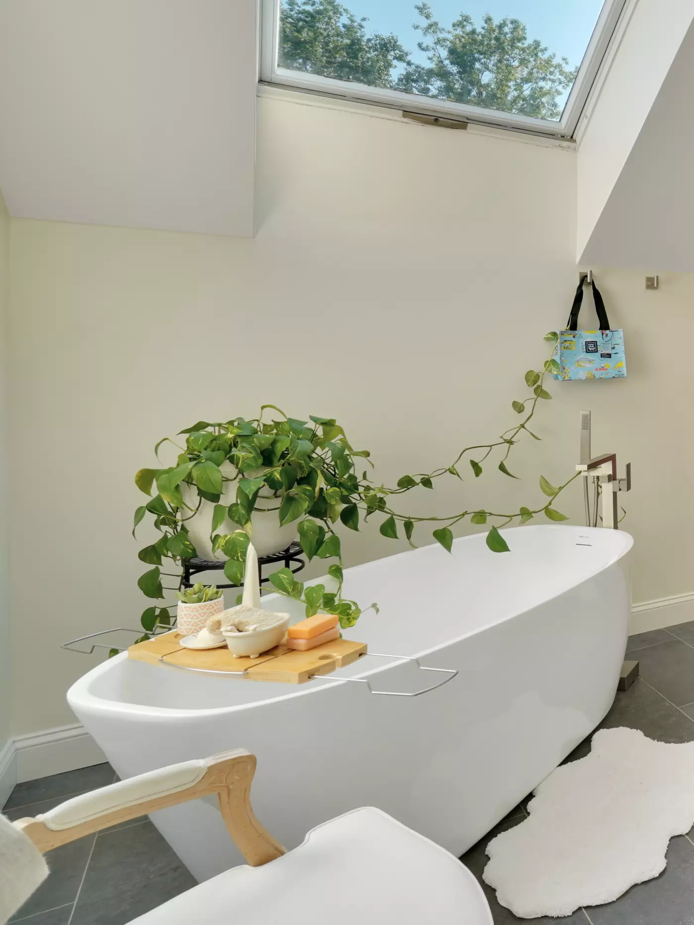 Modern bathroom featuring a freestanding tub, plants, and a wooden tray with bath items.