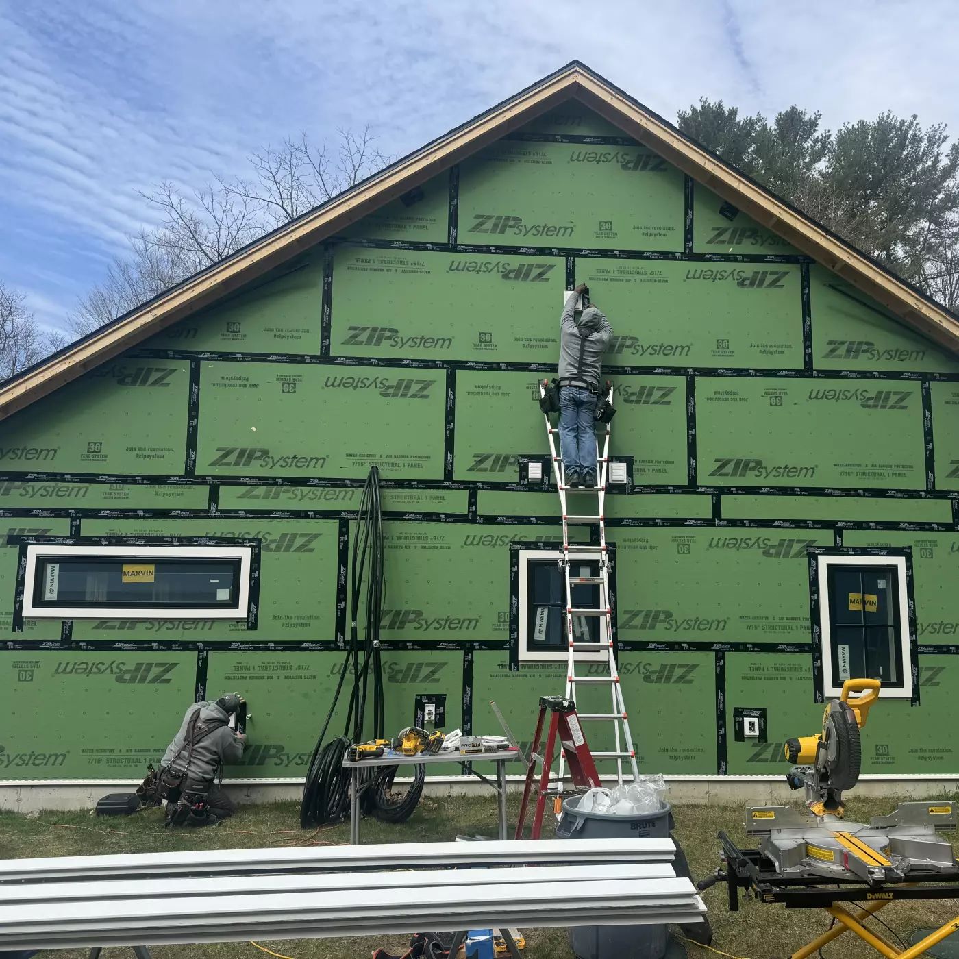 Workers installing green ZIPsystem sheathing on a house under construction.