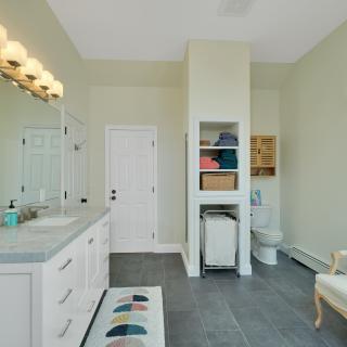 Spacious bathroom featuring a double vanity, storage shelves, and a cozy seating area.