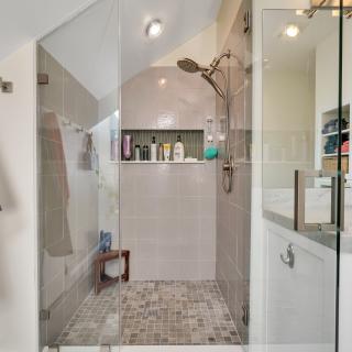 Modern bathroom featuring a glass shower, toiletries, and a gray bathrobe hanging nearby.