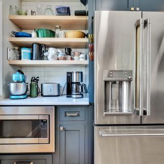 Modern kitchen featuring a stainless steel fridge, microwave, and open shelving with kitchenware.