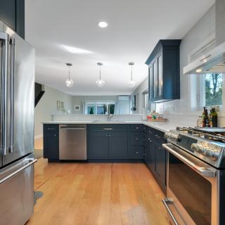 Modern kitchen with stainless steel appliances and navy blue cabinetry on hardwood flooring.