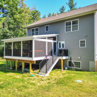 Two-story house with a screened porch, surrounded by greenery and a grassy yard.