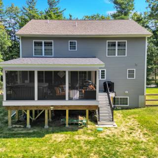 Back view of a grey house with a screened porch and deck, surrounded by trees.