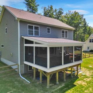 A two-story house featuring a screened porch and nearby grassy area.