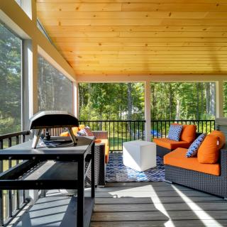 Screened porch with orange chairs, a grill, and a view of the woods.