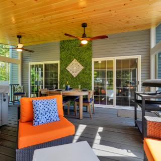Cozy outdoor space with orange seating, dining table, and a grill, surrounded by greenery.