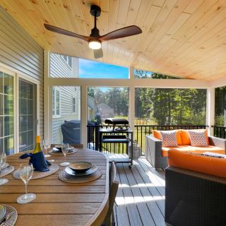 A stylish screened porch with seating, a dining table, and a grill overlooking greenery.