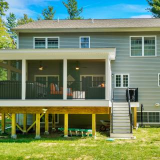 Two-story house with a screened porch, stairs, and green yard in a wooded area.