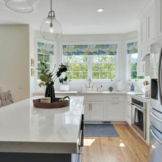 Bright, modern kitchen with white cabinetry, marble island, and large windows.