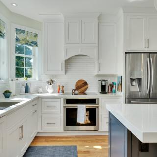 Bright modern kitchen with white cabinets, stainless steel appliances, and large windows.