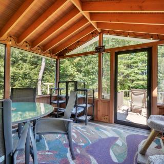 Bright screened porch with wooden beams, seating, and views of greenery outside.