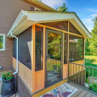 Wood-framed screened porch attached to a beige home with views of the surrounding green landscape.