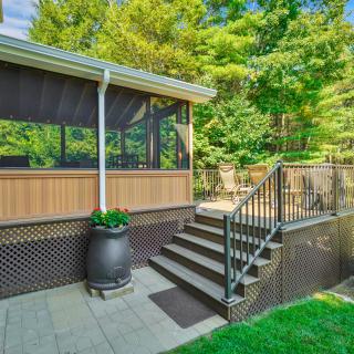Screened porch with wooden steps, black railings, and a large planter surrounded by lush green trees.