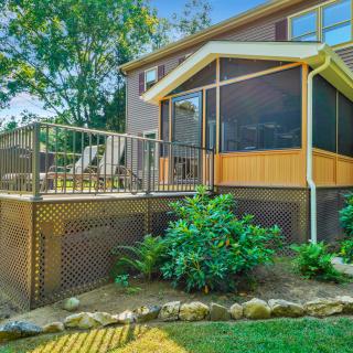 Raised backyard deck with a screened porch, metal railings, lattice skirting, and lush landscaping.